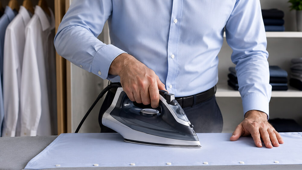 Come stirare una camicia da uomo Uomo che stira correttamente una camicia azzurra su un asse da stiro